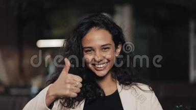 美丽的年轻女子展示拇指向上和微笑站在舒适的咖啡馆。 工作中的少女竖起大拇指